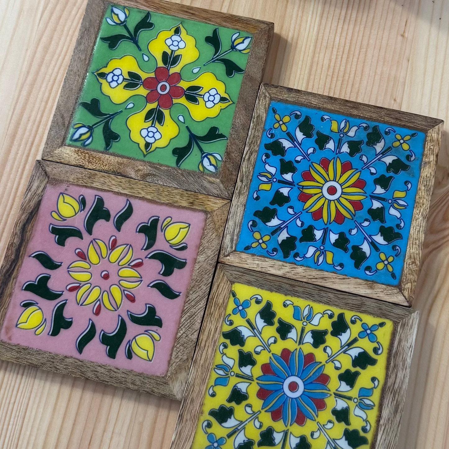 Set of four colorful square coasters with wooden holders on a wooden surface