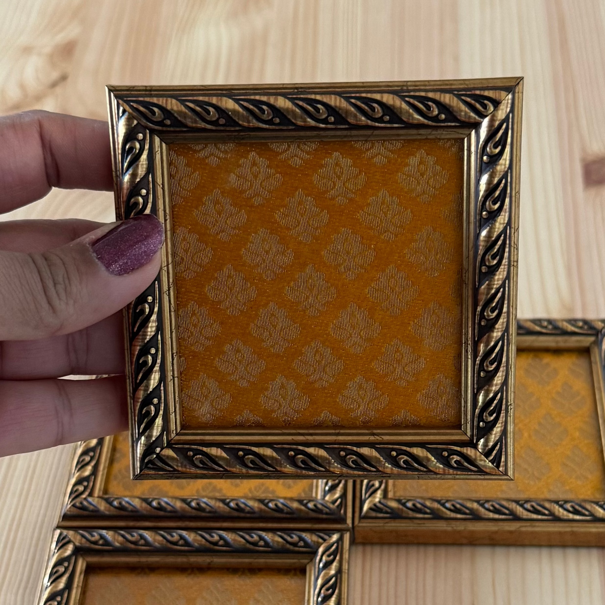 Ornate wooden fame with yellow broade fabric with a hand holding the coaster.
