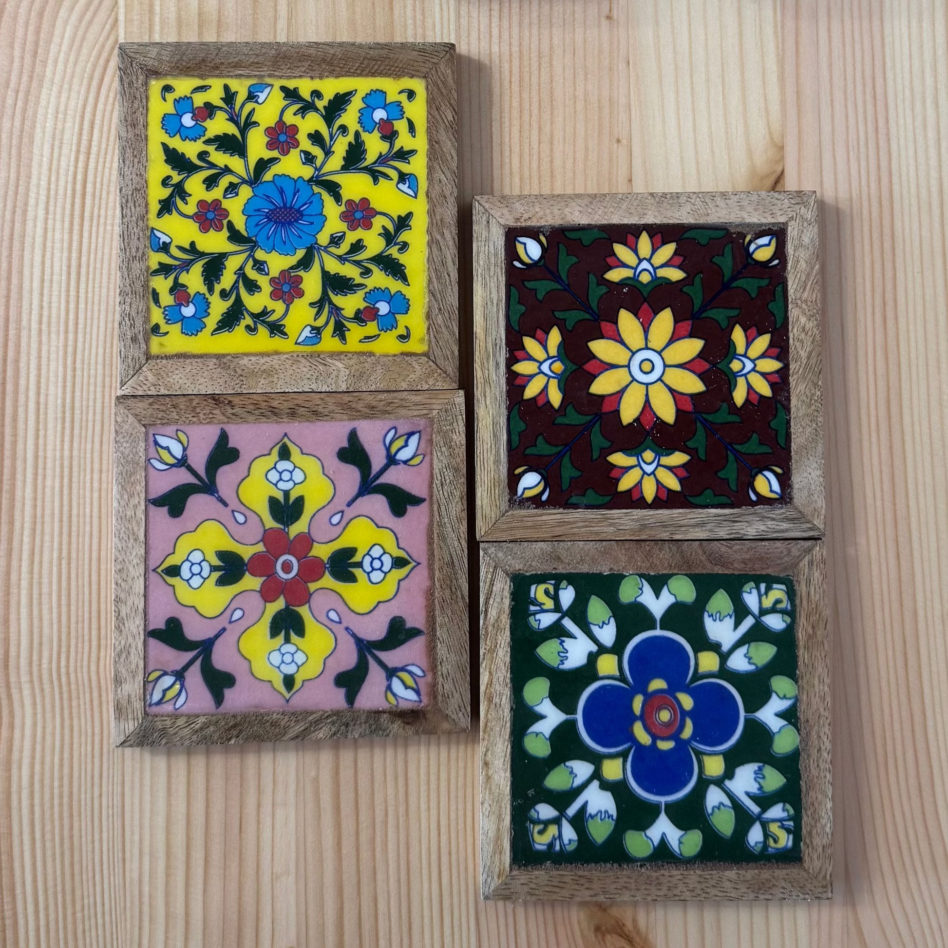 Four colorful square tiles coaster with floral designs on a wooden surface