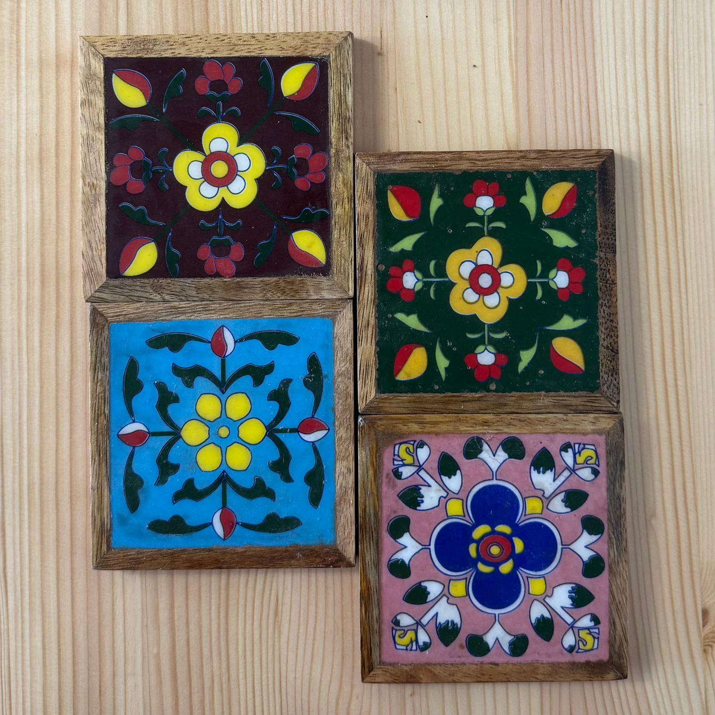 Four square coasters with floral designs in wooden frames on a wooden surface
