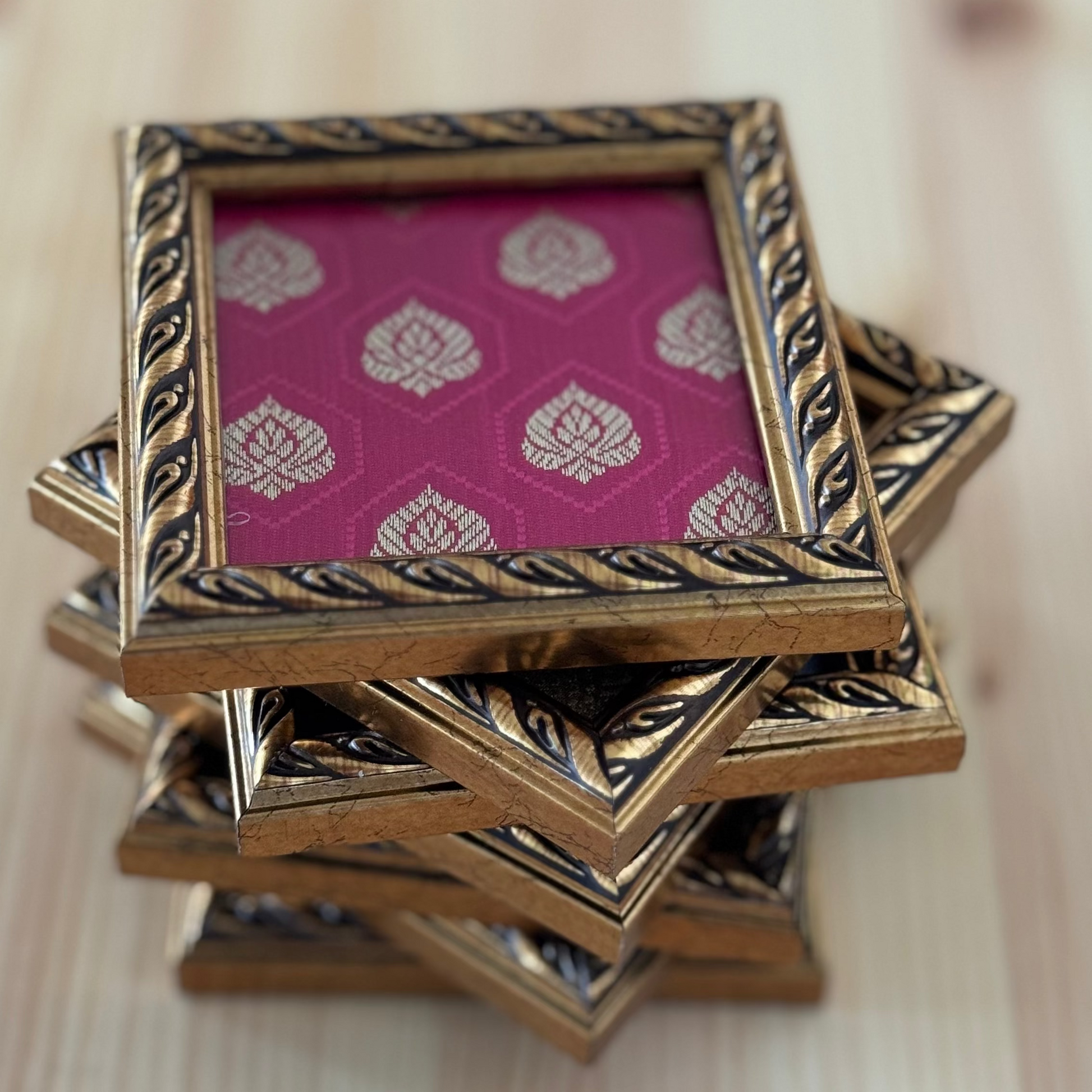 Stack of decorative square fabric coasters with a brocade fabric cover on a wooden table.
