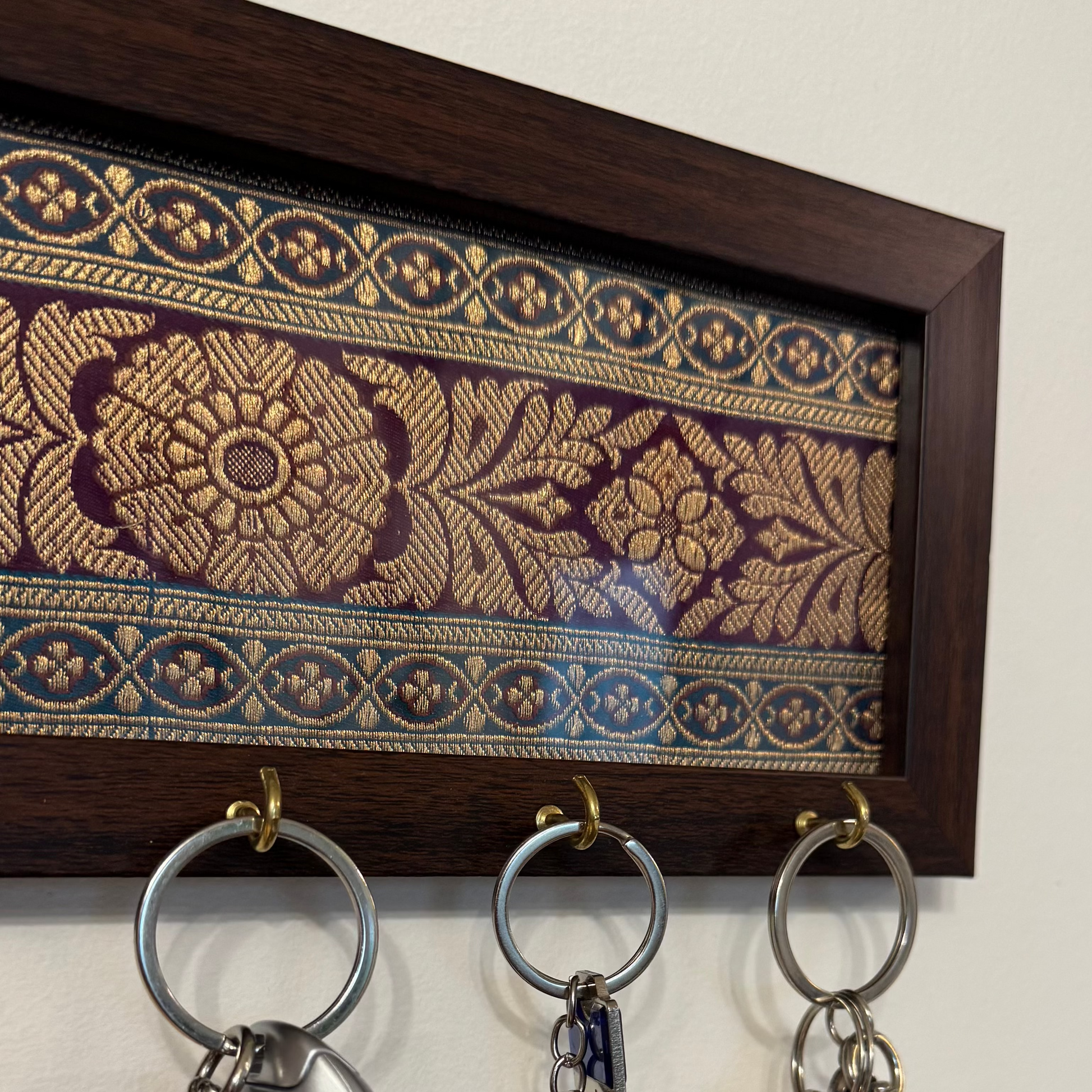 Key holder with keys hanging on a wall, featuring brocade fabric in the background.