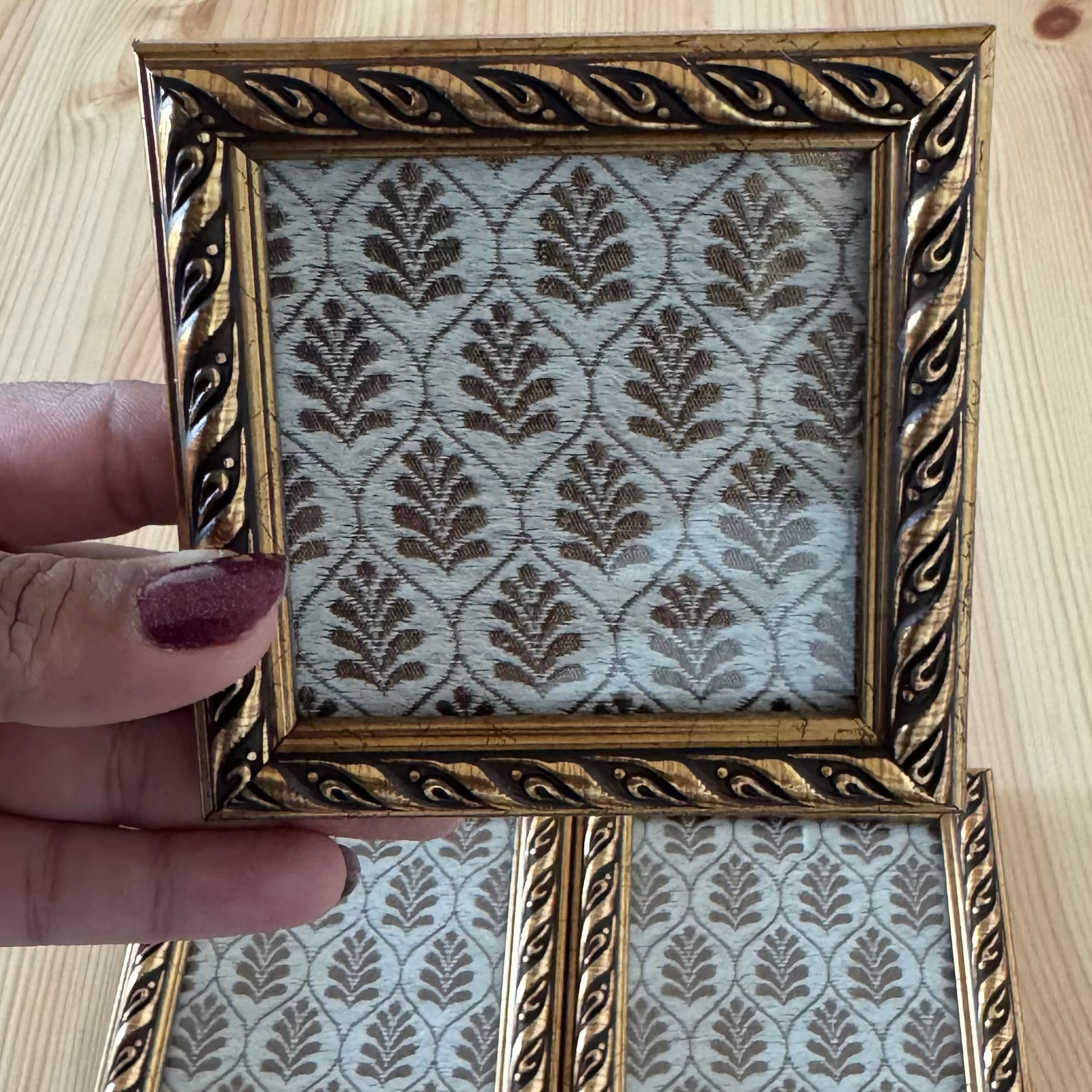 Decorative white and gold coaster with intricate design held by a hand.