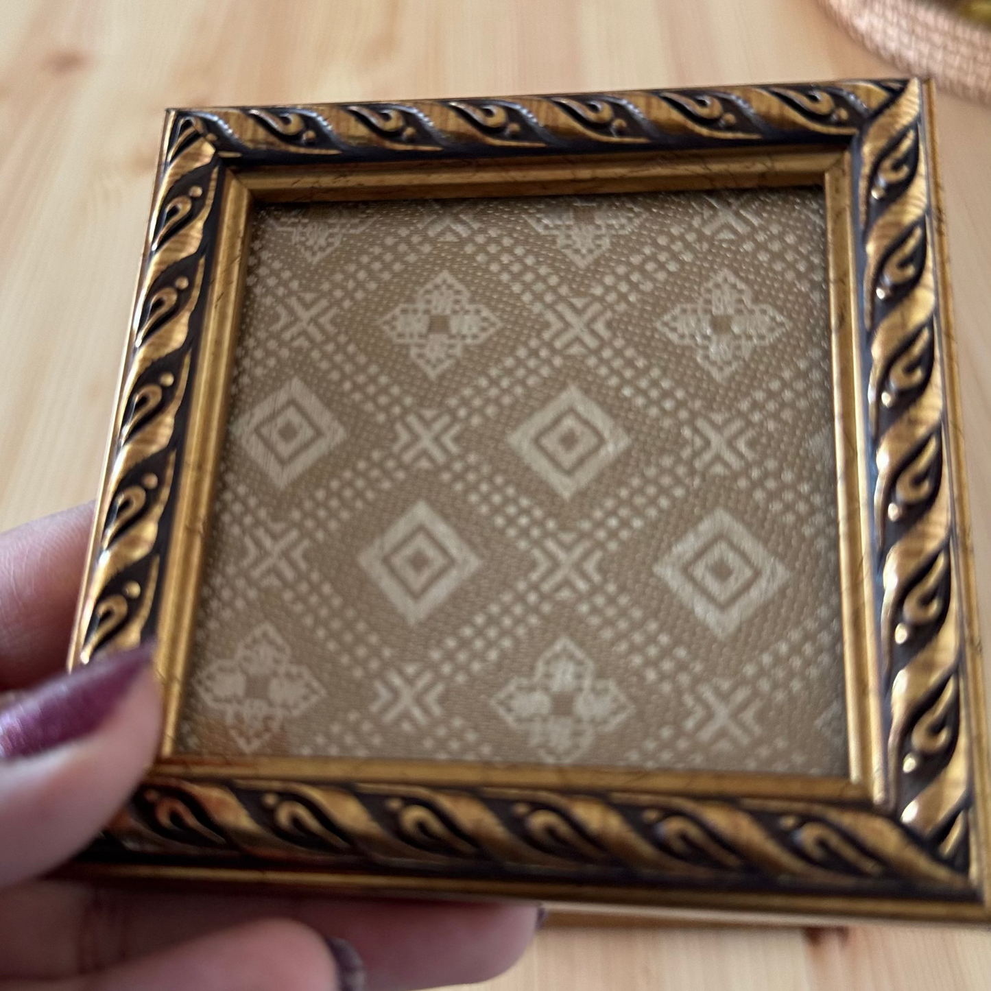 Decorative gold brocade fabric coaster held by a hand.