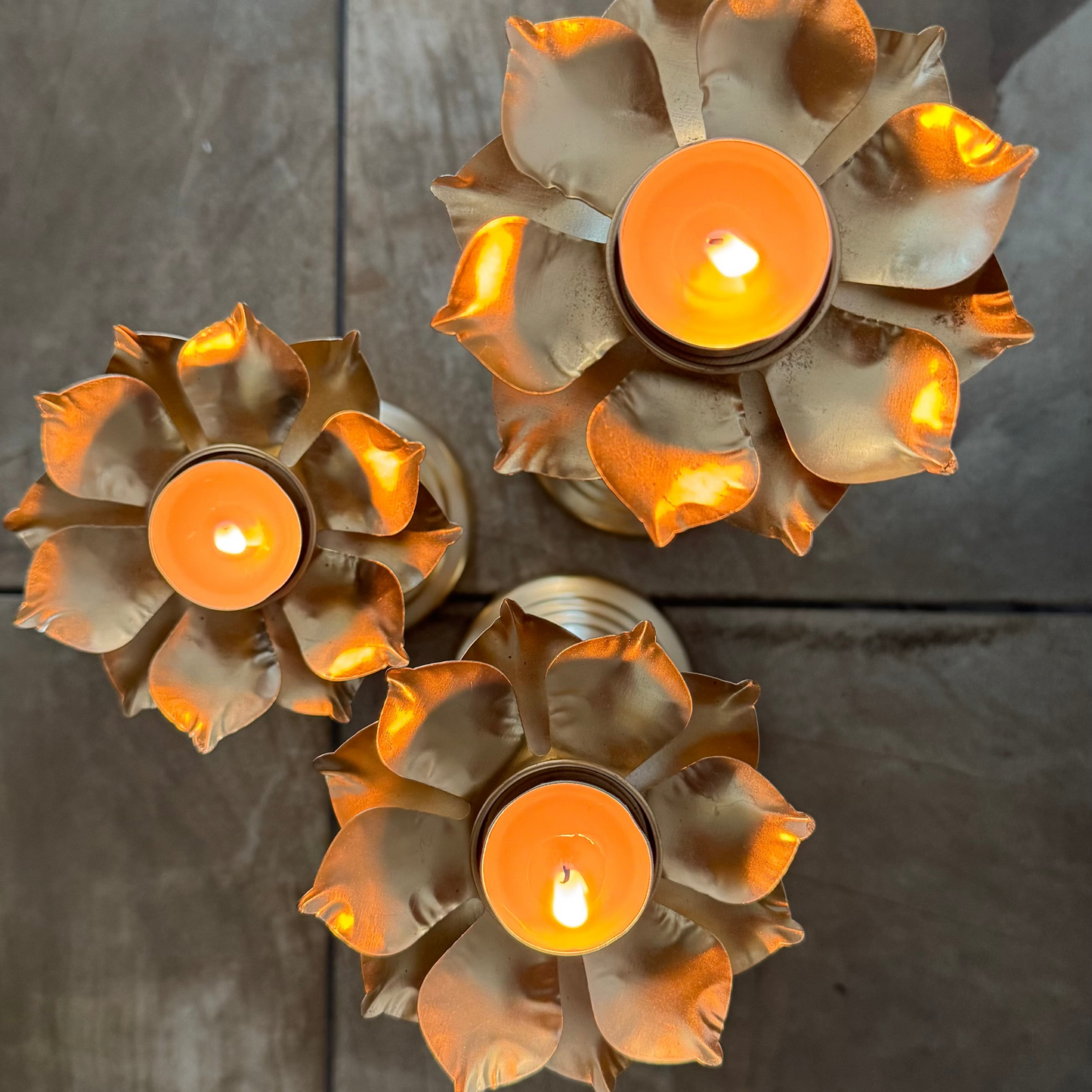 Three lotus tea light candle holders with lit candles on a tiled surface