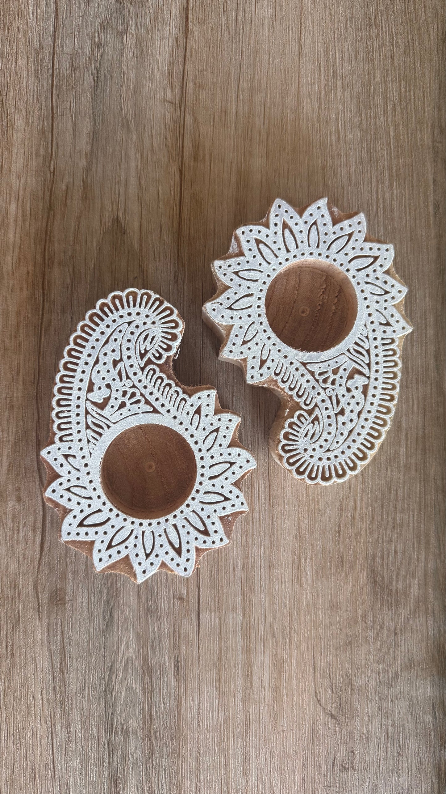 Two wooden ambi paisley tea light holder with intricate white patterns on a wooden surface