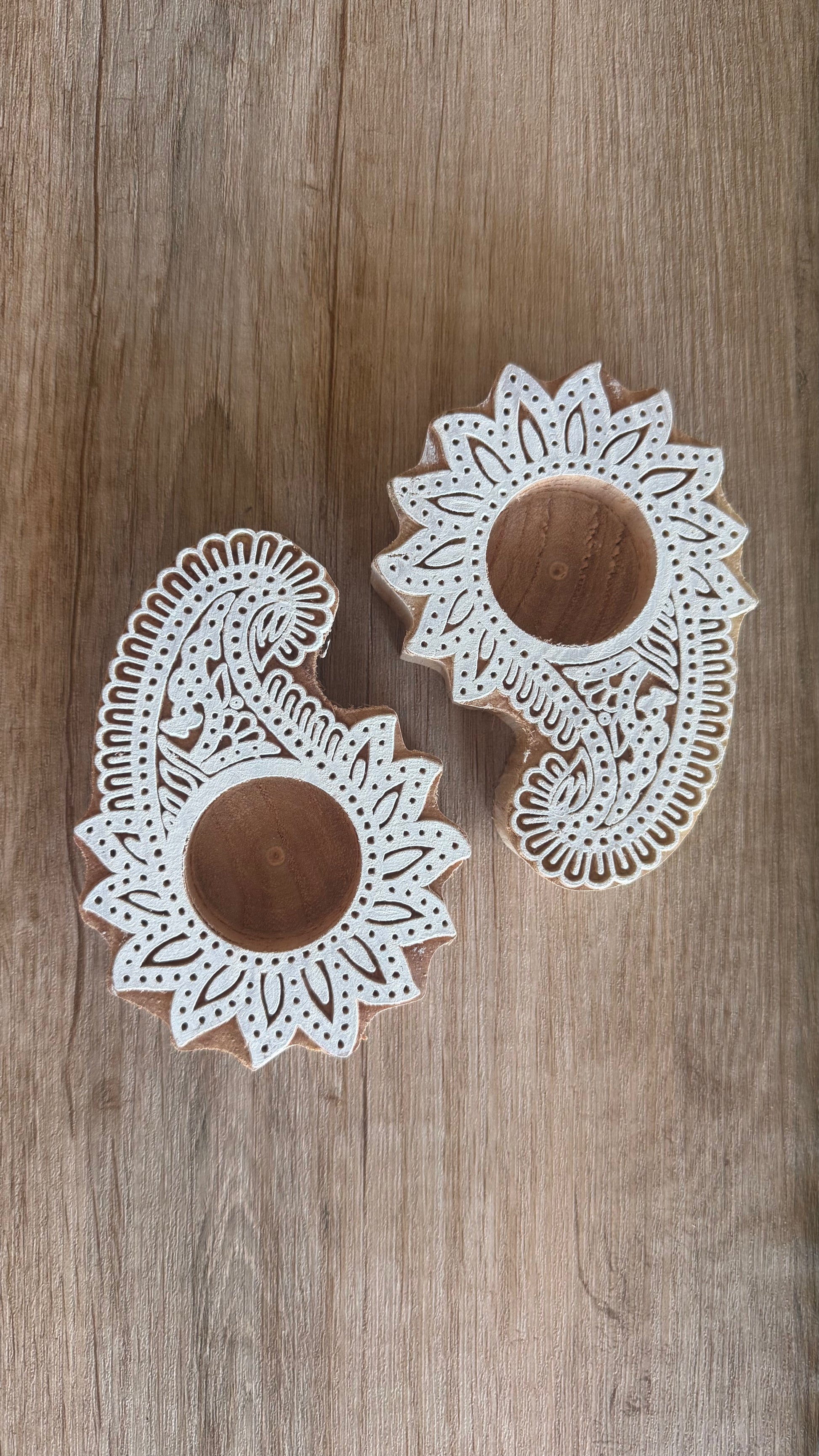 Two wooden ambi paisley tea light holder with intricate white patterns on a wooden surface