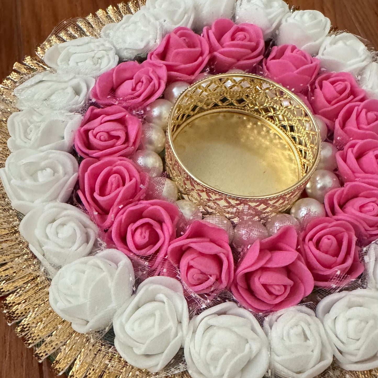 Decorative arrangement of pink and white roses with a gold tea light in the center on a wooden surface.