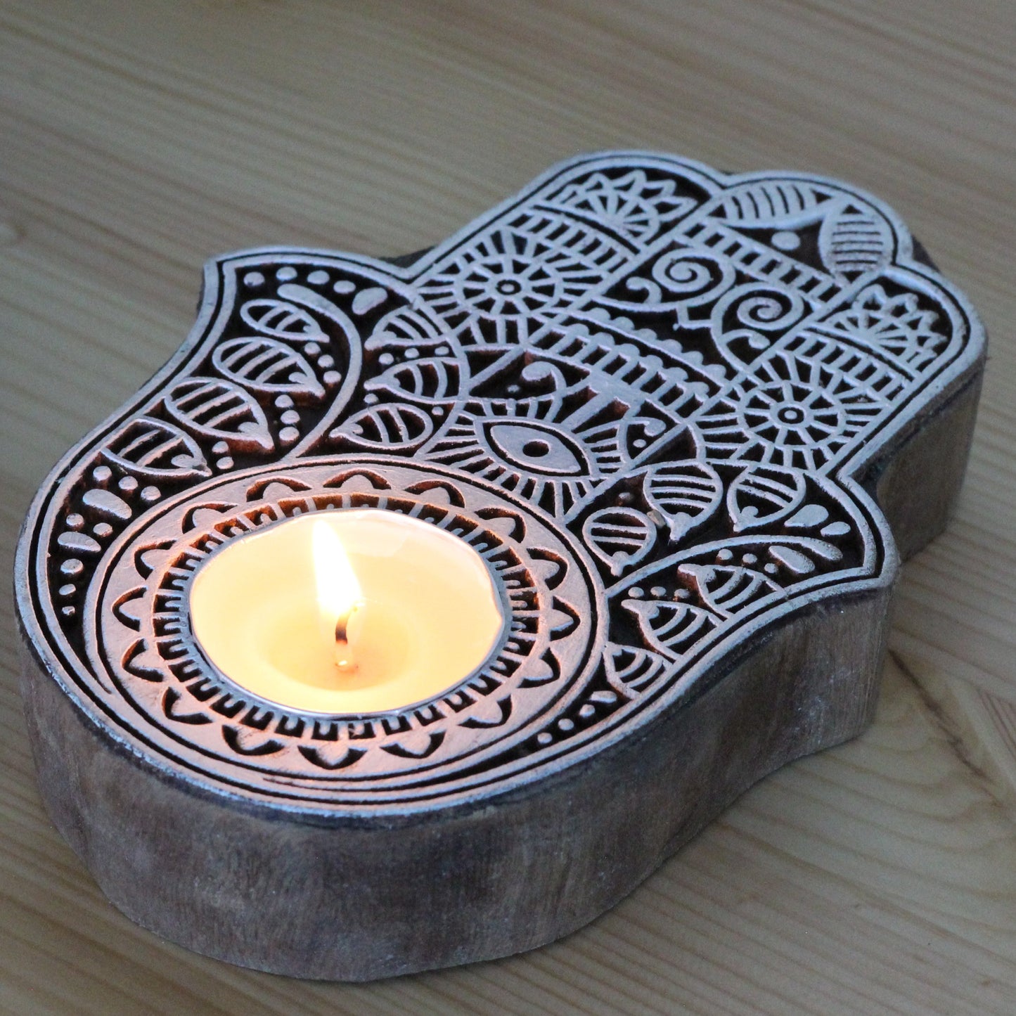 Decorative Hamsa hand candle holder with a lit candle on a wooden surface