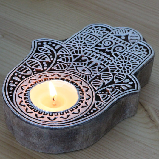 Decorative Hamsa hand candle holder with a lit candle on a wooden surface