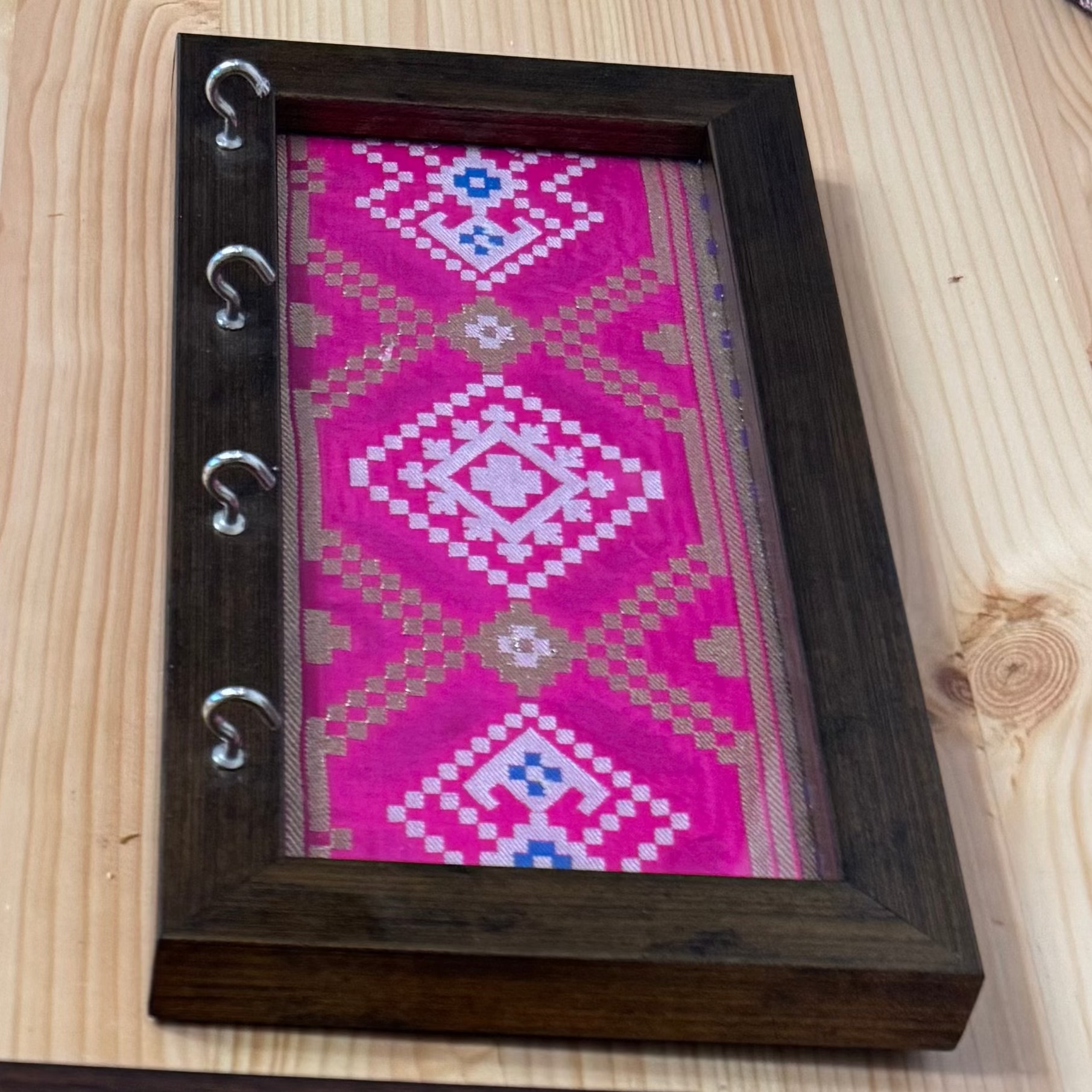 Wooden Framed piece of fabric with intricate patterns with metal hooks.
