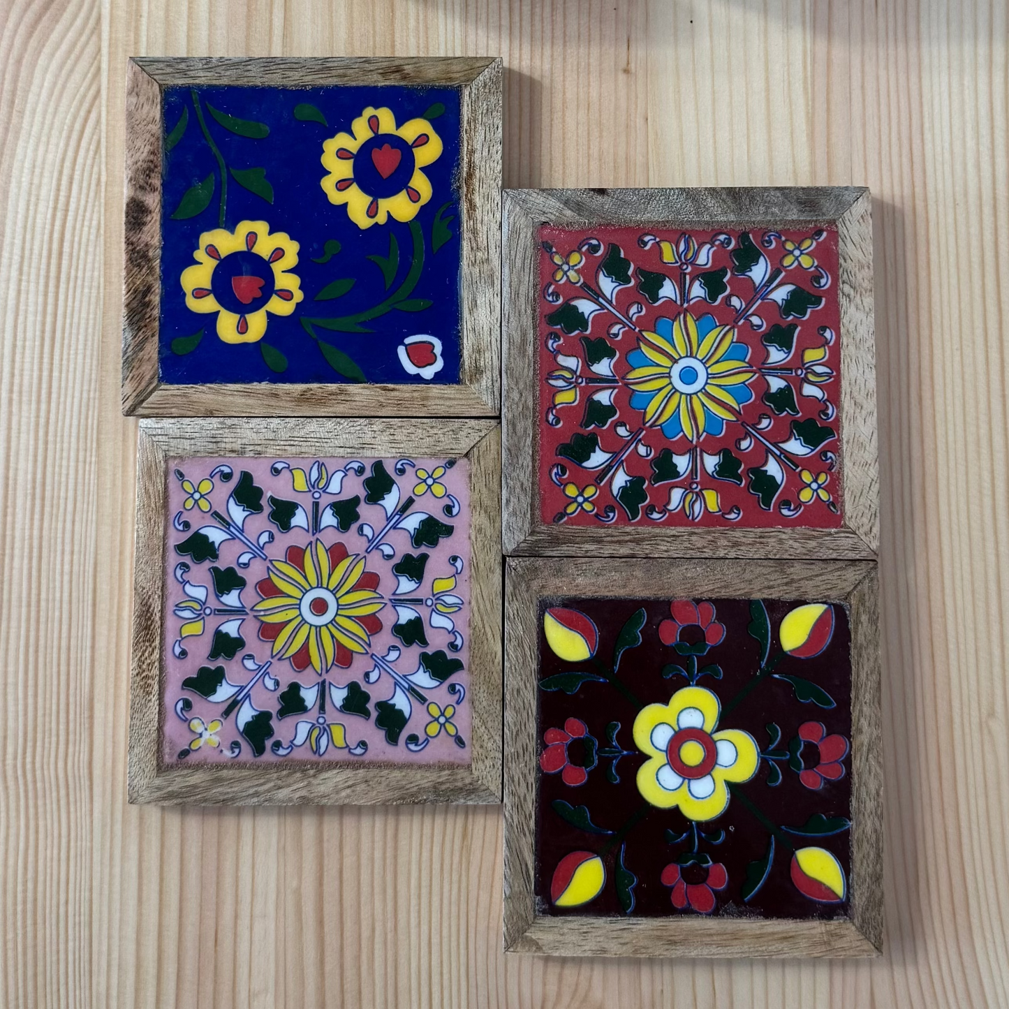 Decorative square coasters with floral patterns in wooden frames on a wooden surface