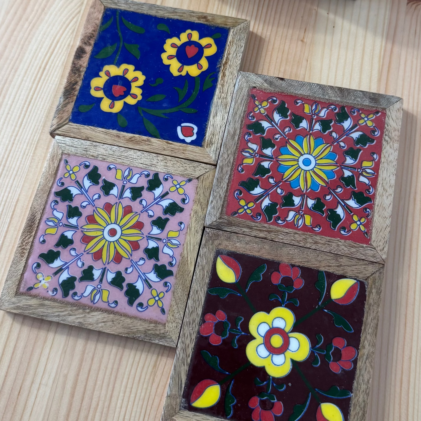 Set of four wooden coasters with floral designs on a wooden surface