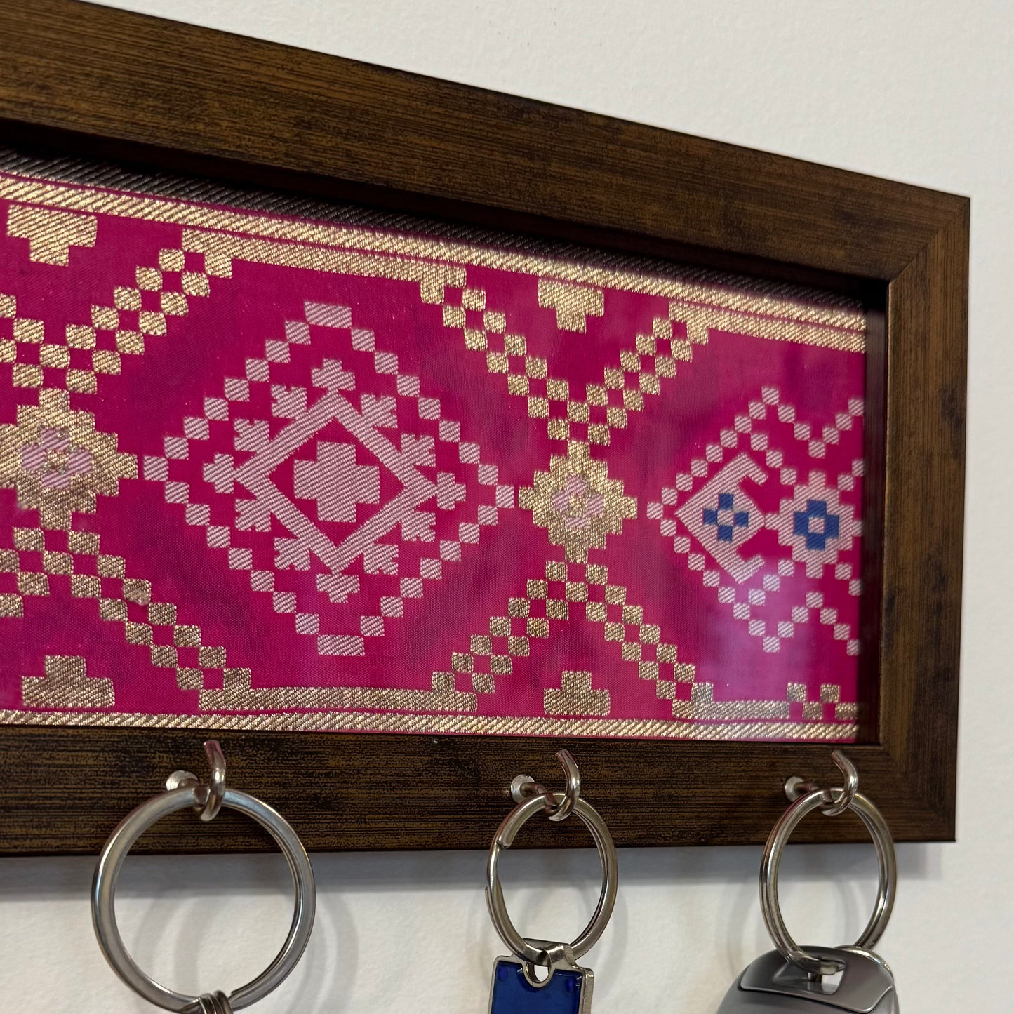 Key holder with keys and a decorative pink and brown patterned board on a white wall.