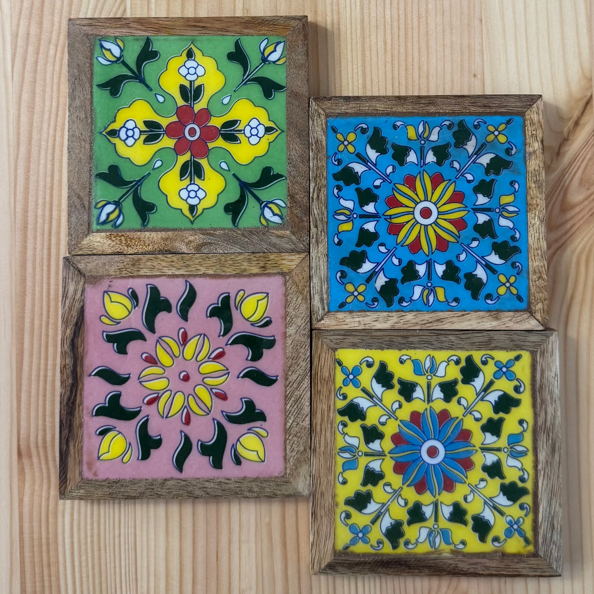 Four colorful square coasters with floral designs on a wooden surface