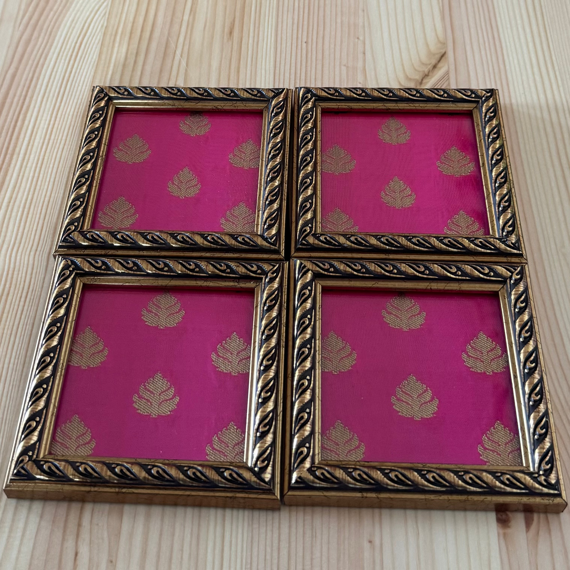 Set of four pink coasters with gold leaf patterns in decorative frames on a wooden surface.