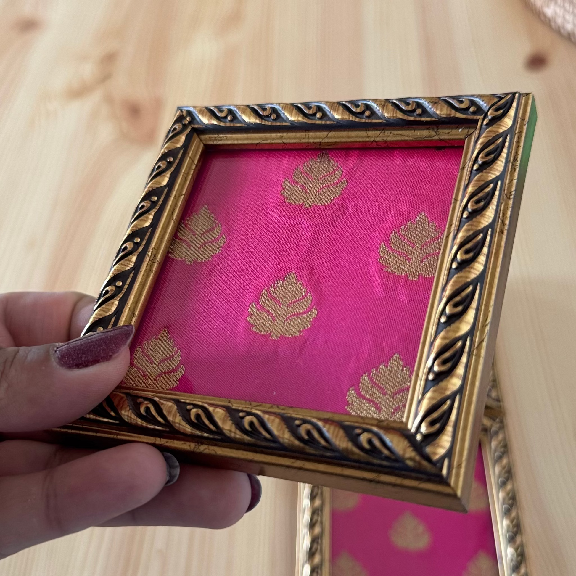 Hand holding a decorative coaster with pink fabric and gold patterns.