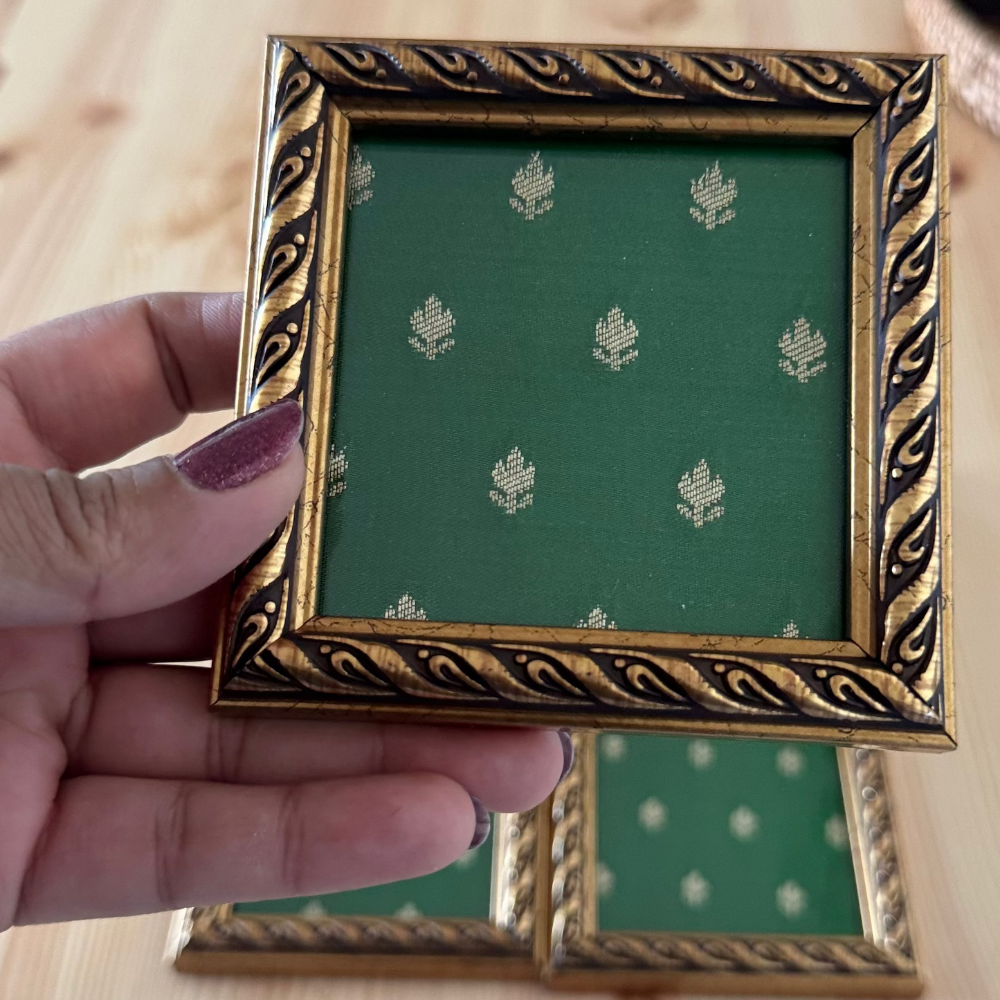 Gold-framed coaster with green brocade fabric held in hand.